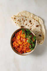 Vegan vegetarian curry with ripe yellow jackfruit served in ceramic bowl with coriander and homemade flatbread flapjack over white marble background. Flat lay, space