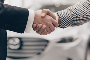 Cropped close up of a handshake of two men at the dealership salon. Salesman shaking hands with his...