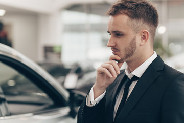 Businessman using his smart phone at the car dealership. Young salesman working at automobile shop, browsing online, using mobile phone. Technology, automotive industry, selling cars concept