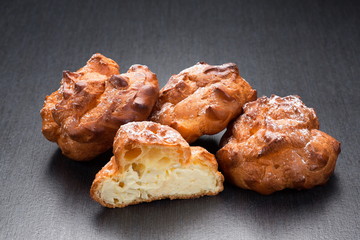 Cream puff french pastry or profiteroles close up. Classical eclairs with vanilla cream on the dark background