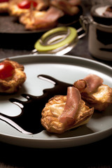 Few puff pastry cups filled by cheese and ham on blue plate with dark sauce