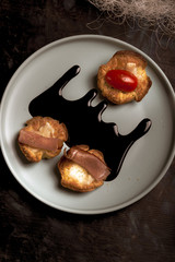 Few puff pastry cups filled by cheese and ham on blue plate with dark sauce