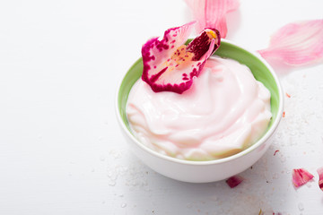 cosmetic cream with pink flower petals, white wood table