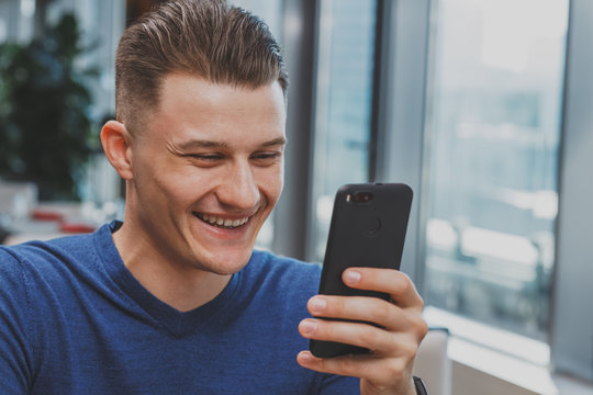 Close up of a handsome happy man laughing reading on his smart phone, copy space. Man smiling cheerfully browsing on his mobile. Attractive man messaging using cell. Technology, online concept - Powered by Adobe