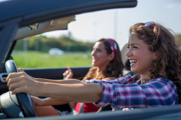 Two young beautiful girls driving in a convertible