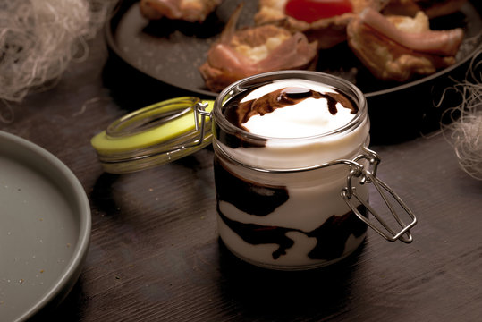 Glass jar with cover full of white and brown sauce on dark wooden board