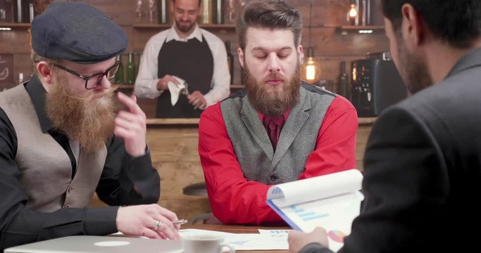 Three Young Marketers Having A Business Meeting In A Local Coffee Shop. Freelancers Discuss Business Durink A Coffee Break.