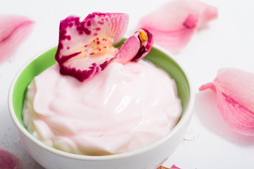 cosmetic cream with pink flower petals, white wood table