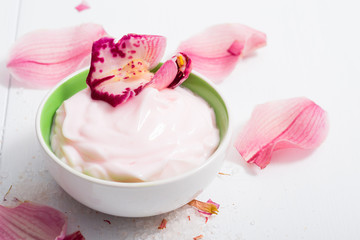 cosmetic cream with pink flower petals, white wood table