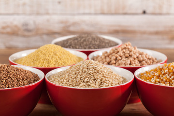 Various grains and cerelas in red bowls on wooden background