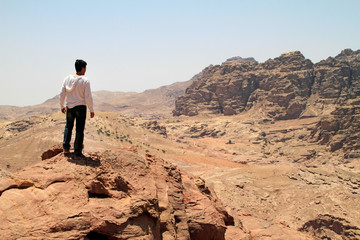 Young man on top of a peak looking over a valley in the rugged landscape of Petra, Jordan