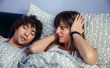 Young man snoring and his wife covering her ears annoyed by the noise