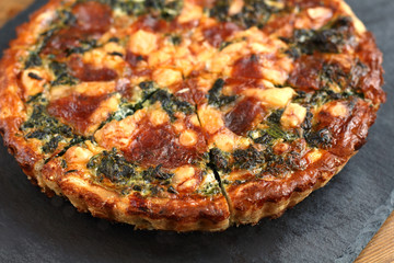 Italian traditional rustic quiche pizza with cheese, spinach  and tomatoes on a black plate in restaurant