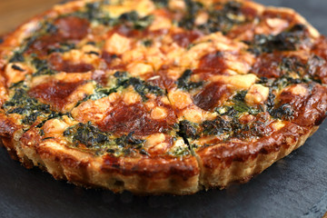 Italian traditional rustic quiche pizza with cheese, spinach  and tomatoes on a black plate in restaurant