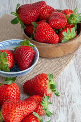 Vertical top view of strawberries in blue bowls and wood on burlap cloth