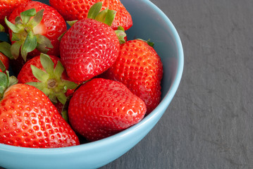 Top view of strawberries in blue bowl on slate stone background