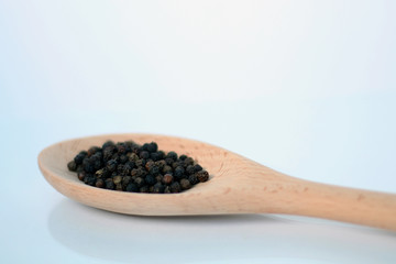 Black pepper in wooden spoon on white background.