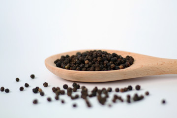Black pepper in wooden spoon isolated on white.