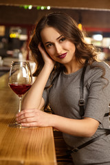 Happy in her own company. Vertical portrait of an attractive young woman having wine at the bar smiling to the camera seductively