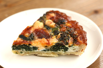 Italian traditional piece of rustic quiche pizza with cheese, spinach  and tomatoes on a white plate in restaurante