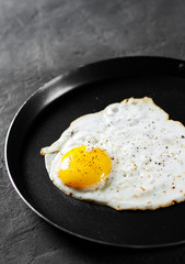 Fried egg in a iron frying pan on Dark grey black slate background