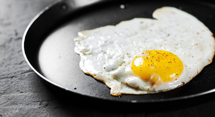Fried egg in a iron frying pan on Dark grey black slate background