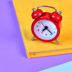 Red alarm clock on a colorful office paper as a symbol of time