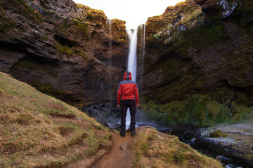 Man standing in front of Kvernufoss waterfall and looking into the cascade during a winter sunrise. Long exposure photo of this hidden waterfall in southern Iceland. 