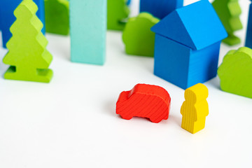 Insurance or business concept. Wooden person with a car on the street of City with wooden blocks houses on the background.. Miniature people 
