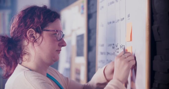 Young woman is sticking sticky notes on whiteboard