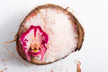 pile of pink bath salt with orchid flower at coconut shell bowl, white wood table