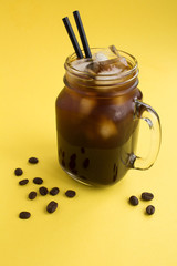 Iced coffee in the glass on the yellow background