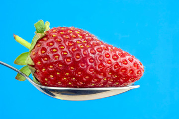 Healthy strawberry in spoon on blue background