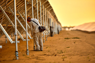 Asian engineer patrolling the desert solar photovoltaic power station in the sunset