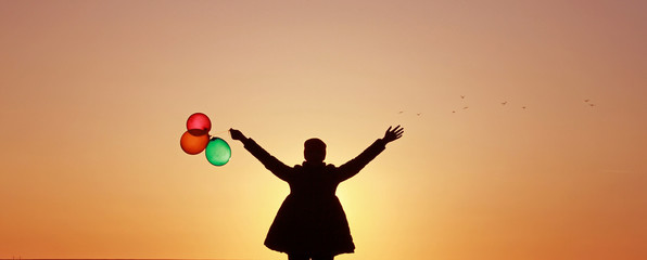 Fototapeta na wymiar The girl with colorful balloons on the background of the sunset