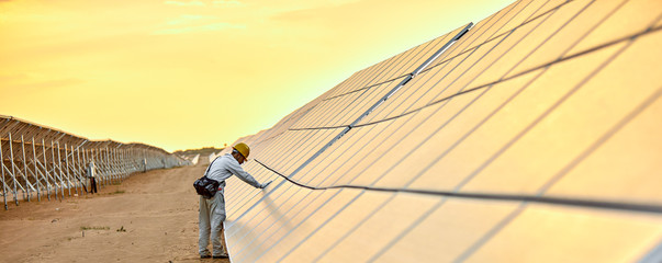 Asian engineer patrolling the desert solar photovoltaic power station in the sunset