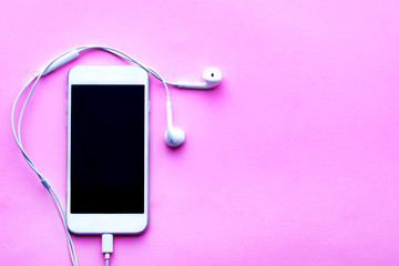 White smartphone with headphones connected on a pink background. View from above.