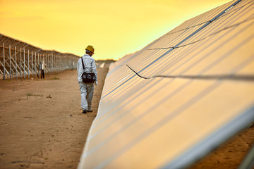 Asian engineer patrolling the desert solar photovoltaic power station in the sunset