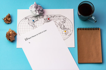 The inscription on a white sheet of A4: 10 best plases to visit in live. On a blue background with a cup of coffee, a notepad and a map of the world.