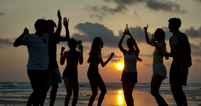Slow motion of silhouette group of young people dancing at beach party on sunset.