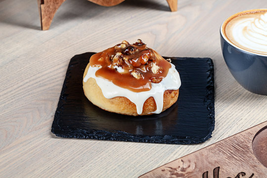 Close up view on fresh homemade  cinnabon bun with toping caramel and nuts. Sweet morning with coffee. Bakery with copy space. Sweet dessert for cooking book or recipe