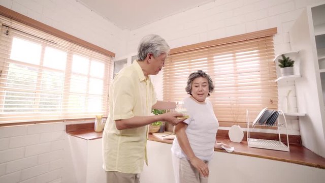 Asian Elderly Couple Man Holding Cake Celebrating Wife's Birthday In Kitchen At Home. Chinese Couple Enjoy Love Moment Together At Home. Lifestyle Senior Family At Home Concept.