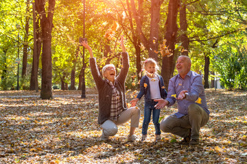 Grandparents and grandchild throwing leaves in park and having fun together