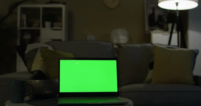 Close up of the Interior of the laptop computer with green screen on the coffee table in the middle of the living room in the evening. Indoors. Alpha channel. Chroma key. Interior at night.