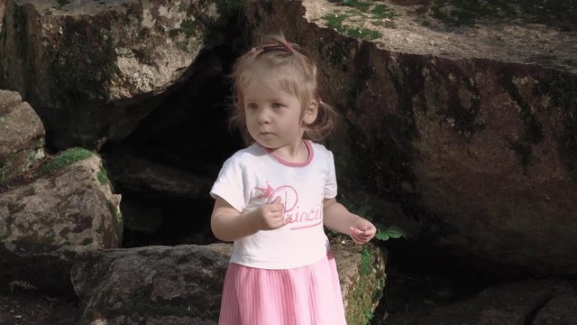 Portrait of little girl near big stones in forest, which looks for something, close-up