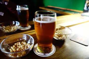 Pale IPA beer in a pint glass with salty peanuts and pistachios