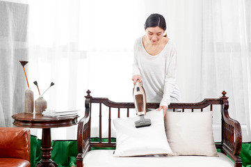 Asian girl uses a wireless vacuum cleaner to clean the dust in the pillow