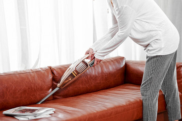 Asian girl uses a wireless vacuum cleaner to clean the gap of the sofa