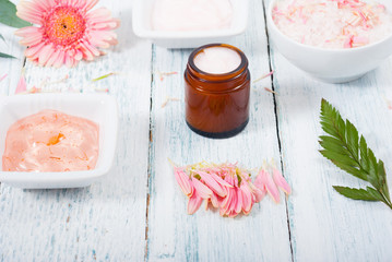 Fototapeta na wymiar beauty product samples, cosmetic cream, bath salt, liquid soap and pink flower, white wood table