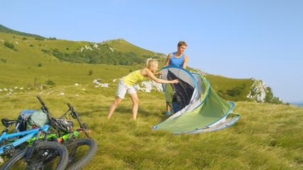 Active sporty couple mountain biking in the Alps setting up their pop up tent.